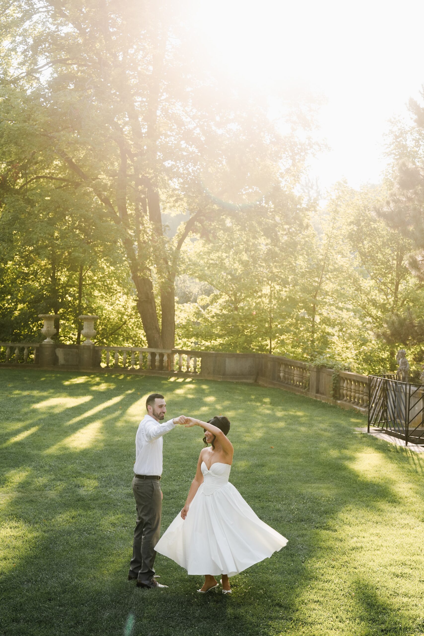 Bride and groom dancing outdoors in sunlight.