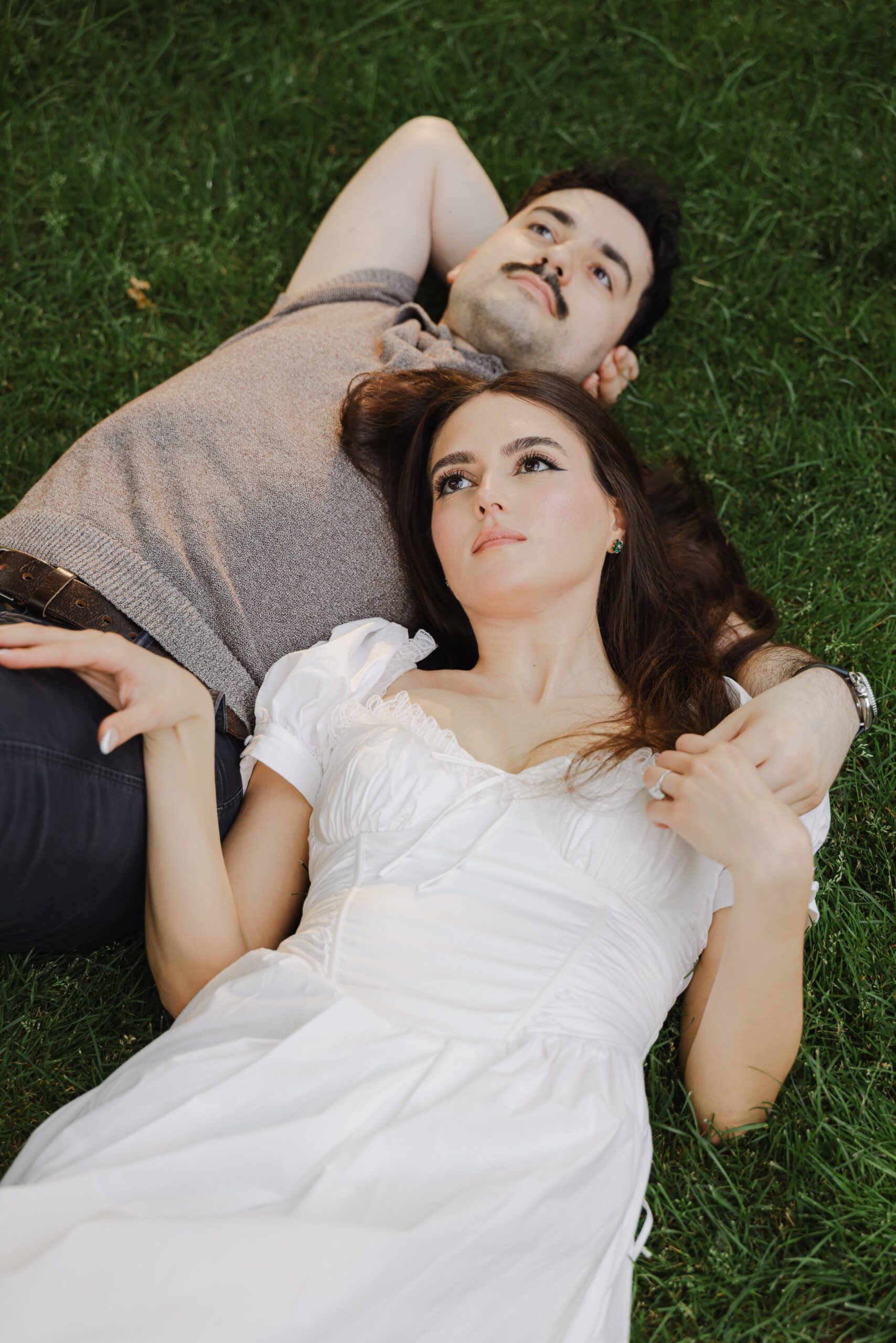 A couple lying on grass, looking thoughtfully upward.