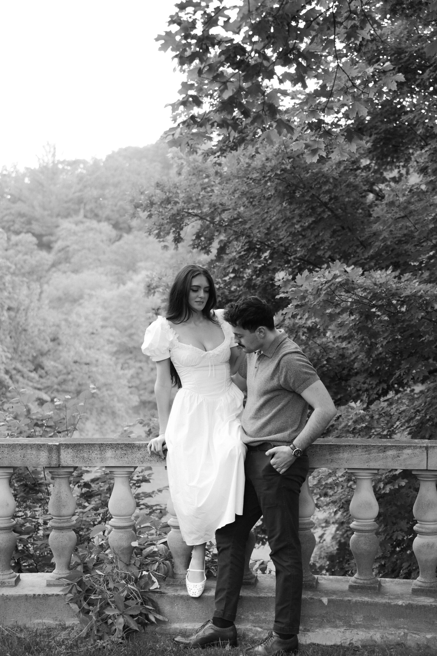 A couple shares a tender moment outdoors near a stone railing.