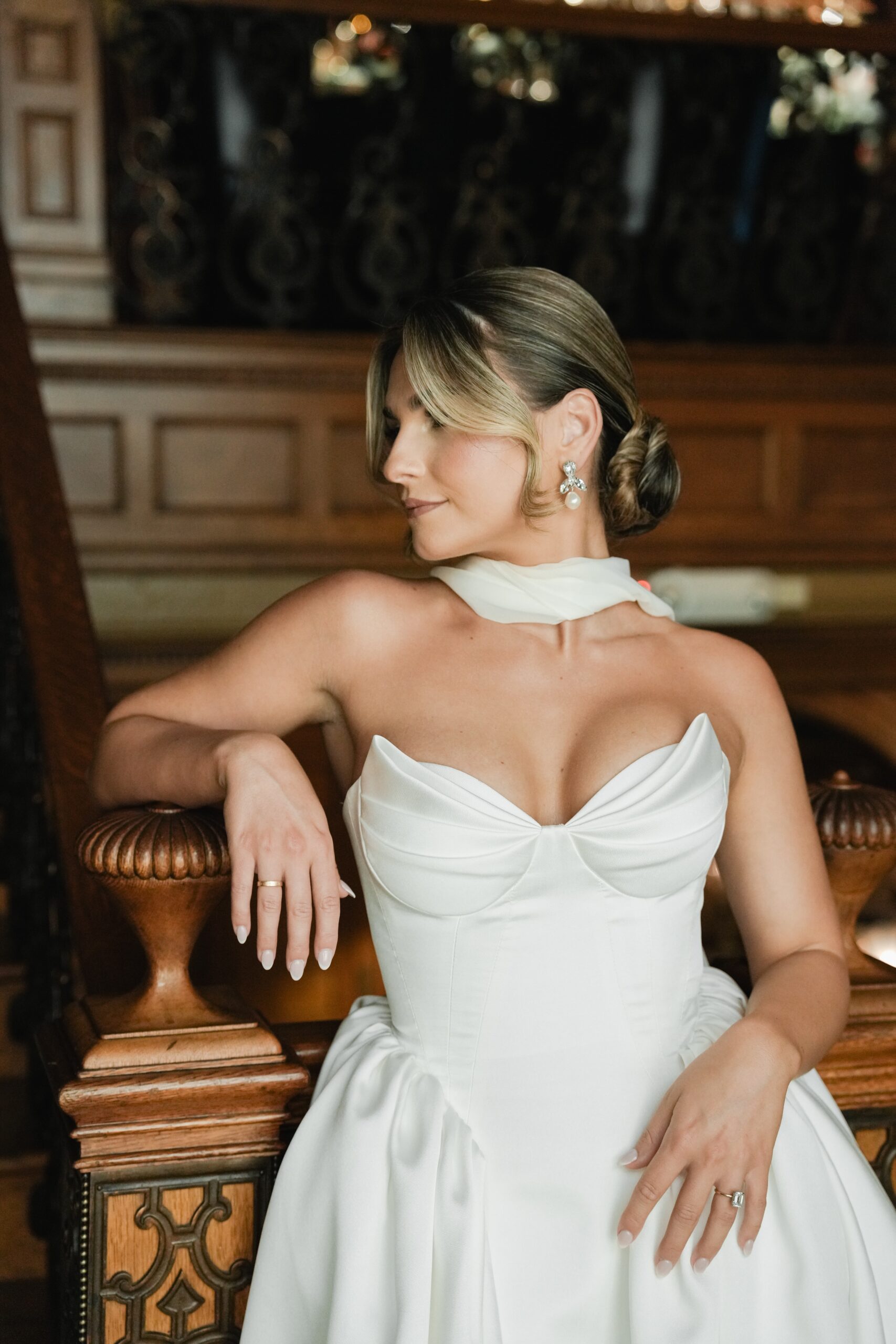 Woman in elegant white dress sitting on a wooden chair.