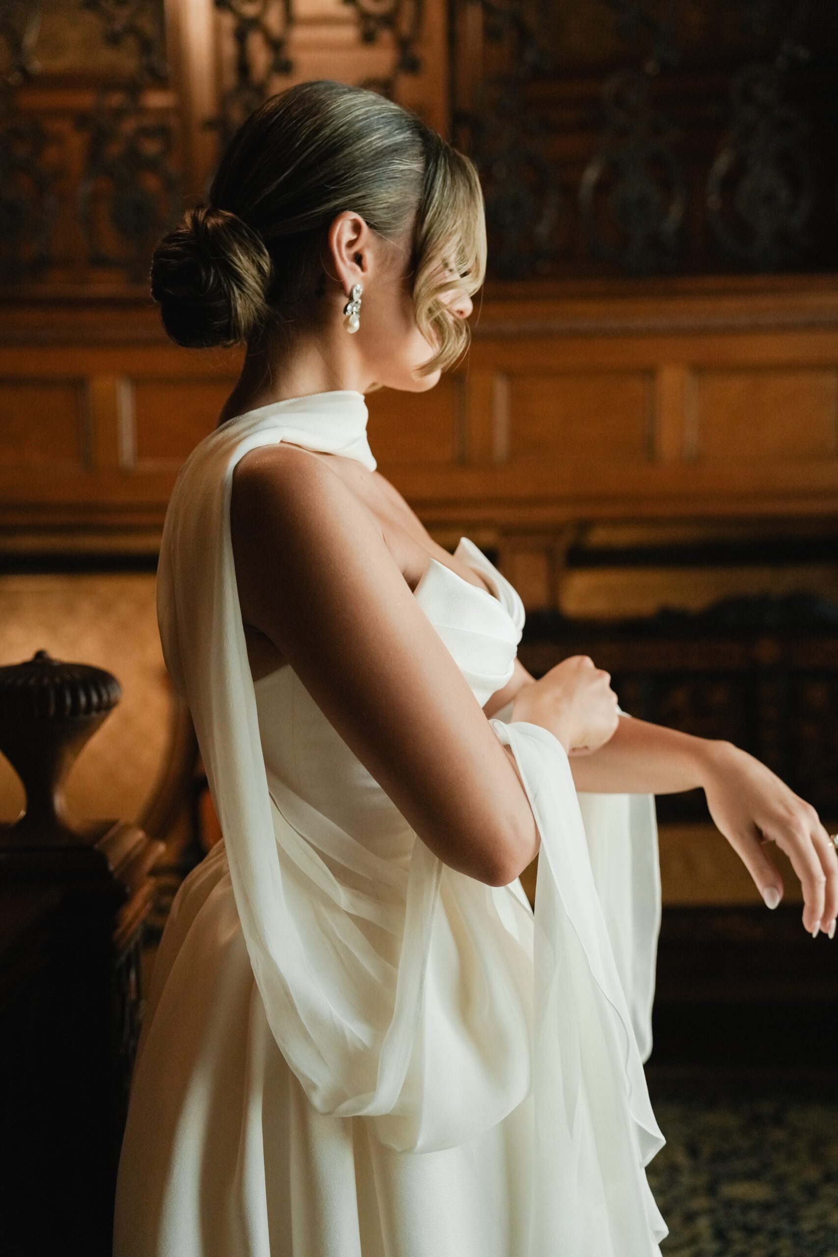Bride in a white wedding dress adjusting her veil indoors.
