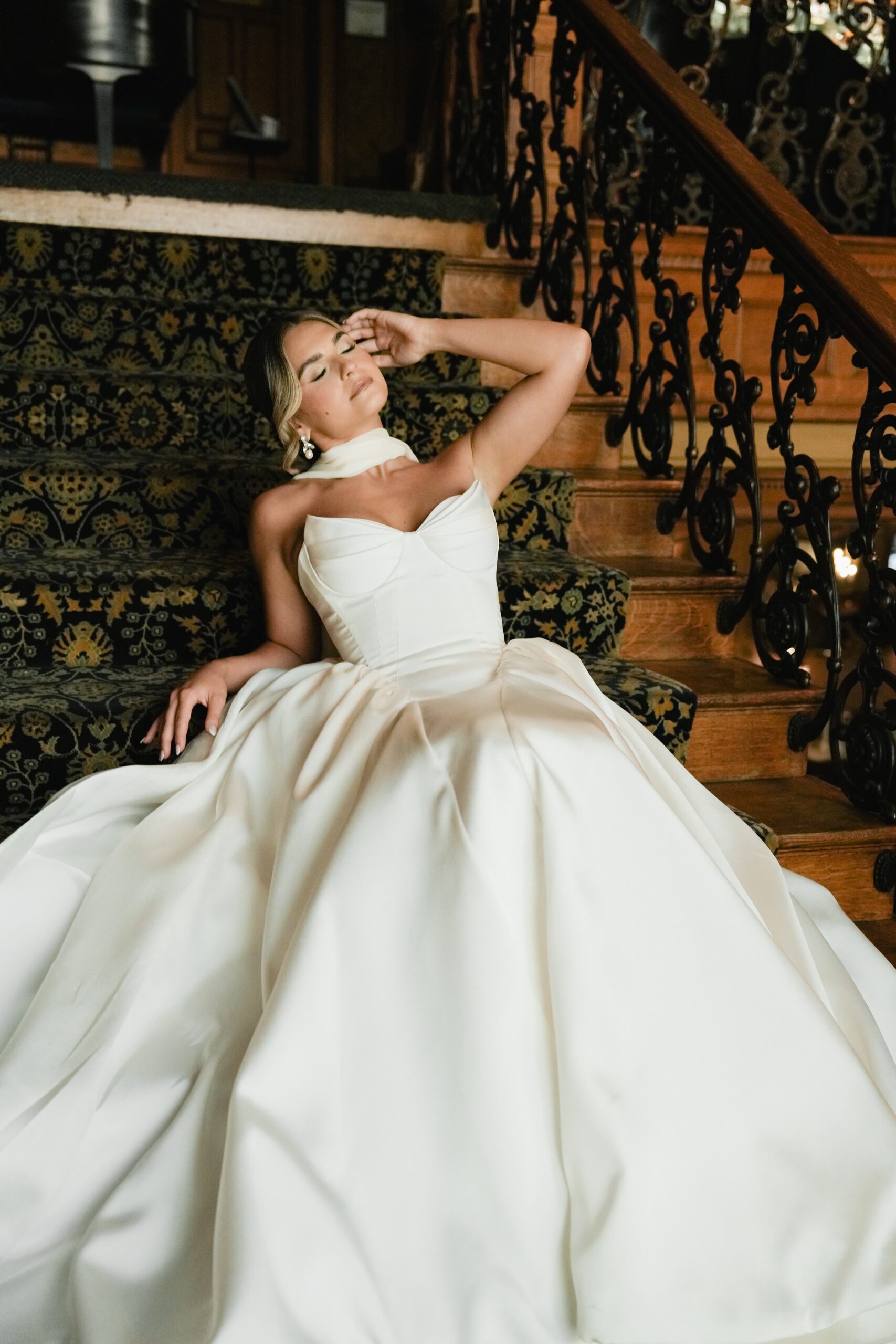 Elegant bride posing gracefully on staircase in a stunning white gown.