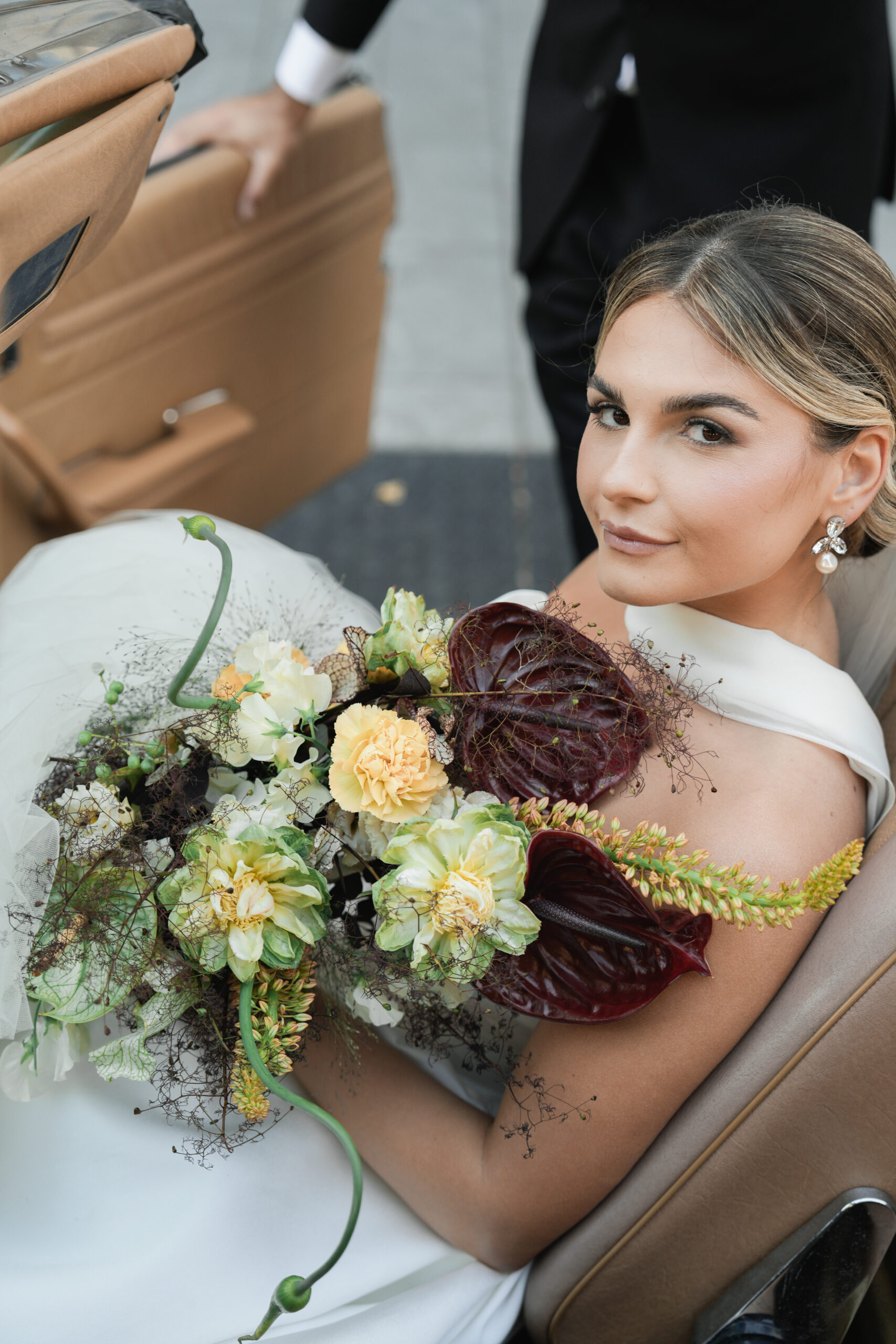 Bride holding a bouquet of roses and greenery, looking up.