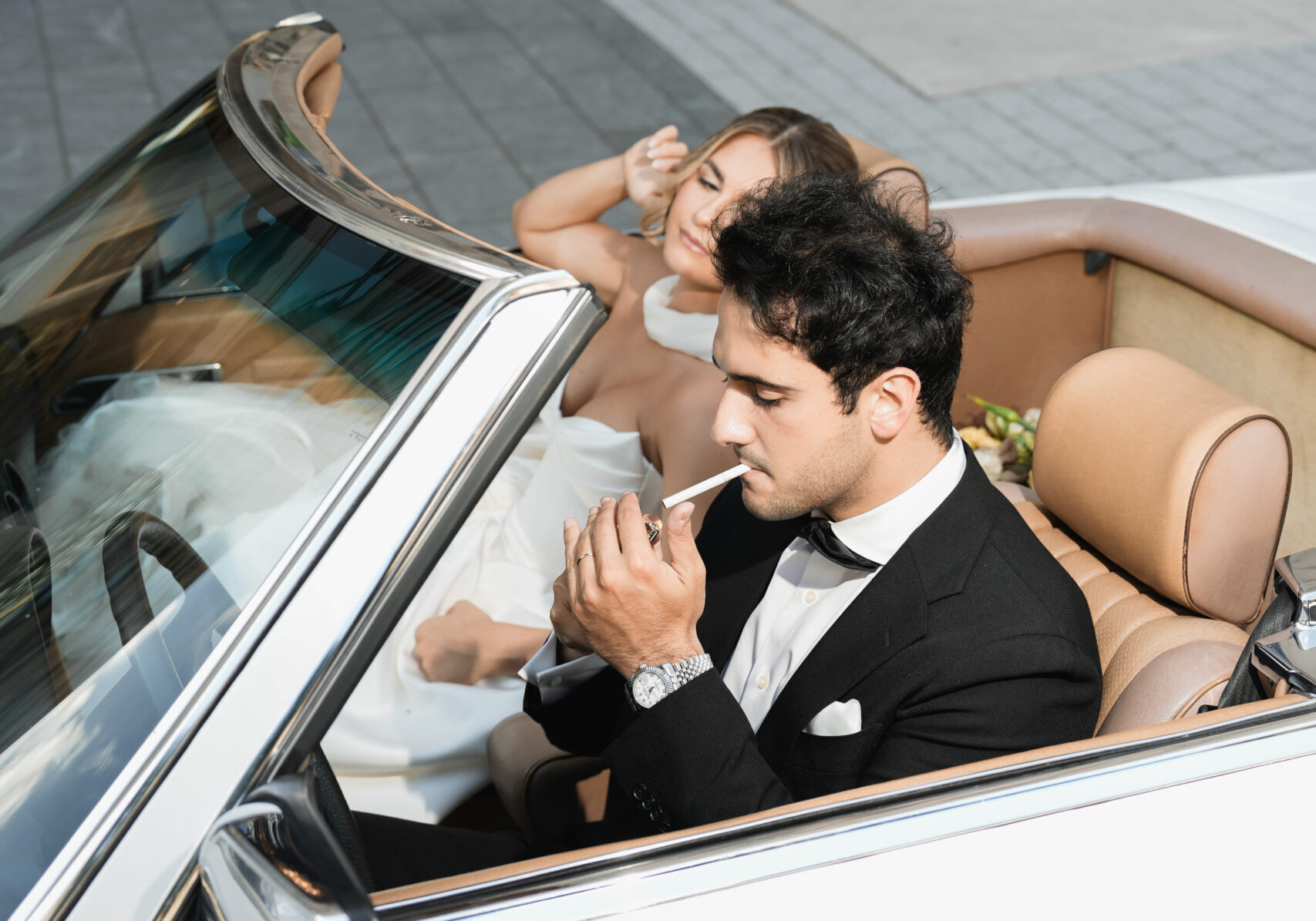 Stylish couple in a convertible, man lighting a cigarette.