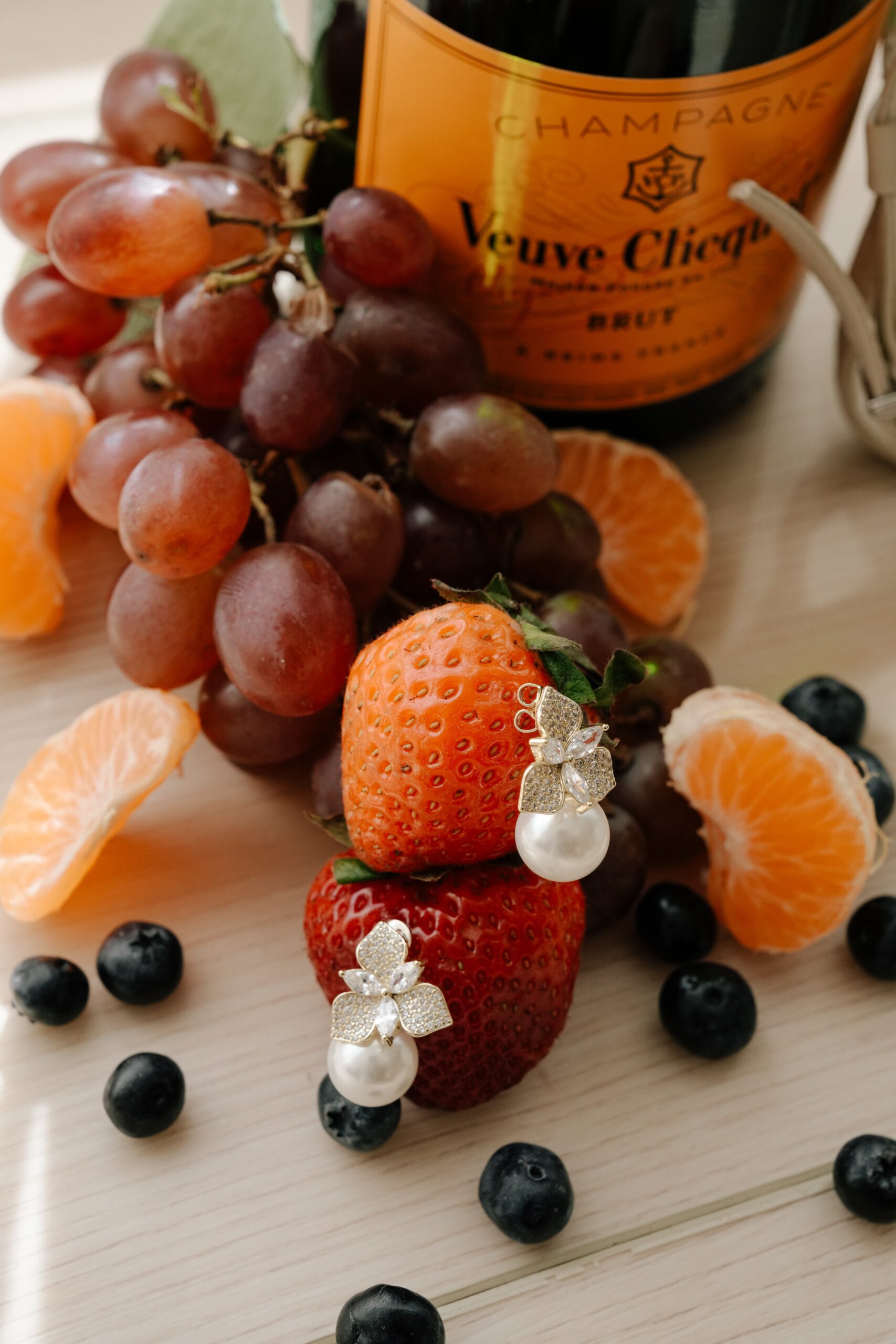 Fresh berries and citrus slices with pearl earrings on a wooden surface.