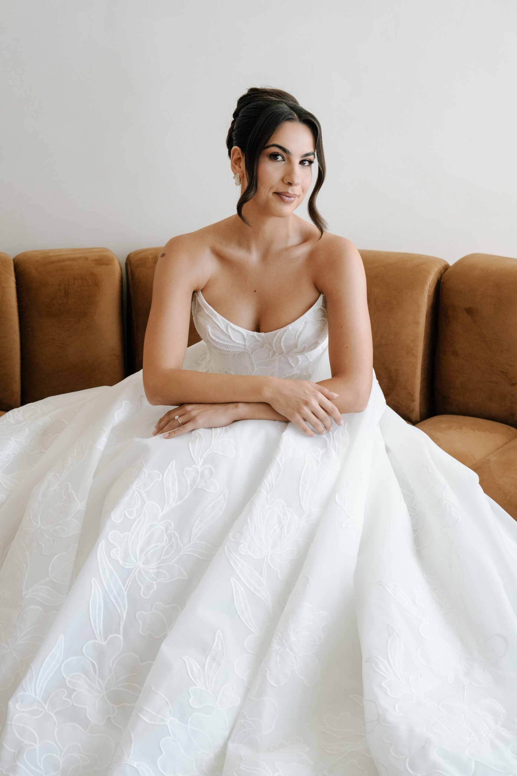Bride in a white wedding dress sitting on a brown sofa.