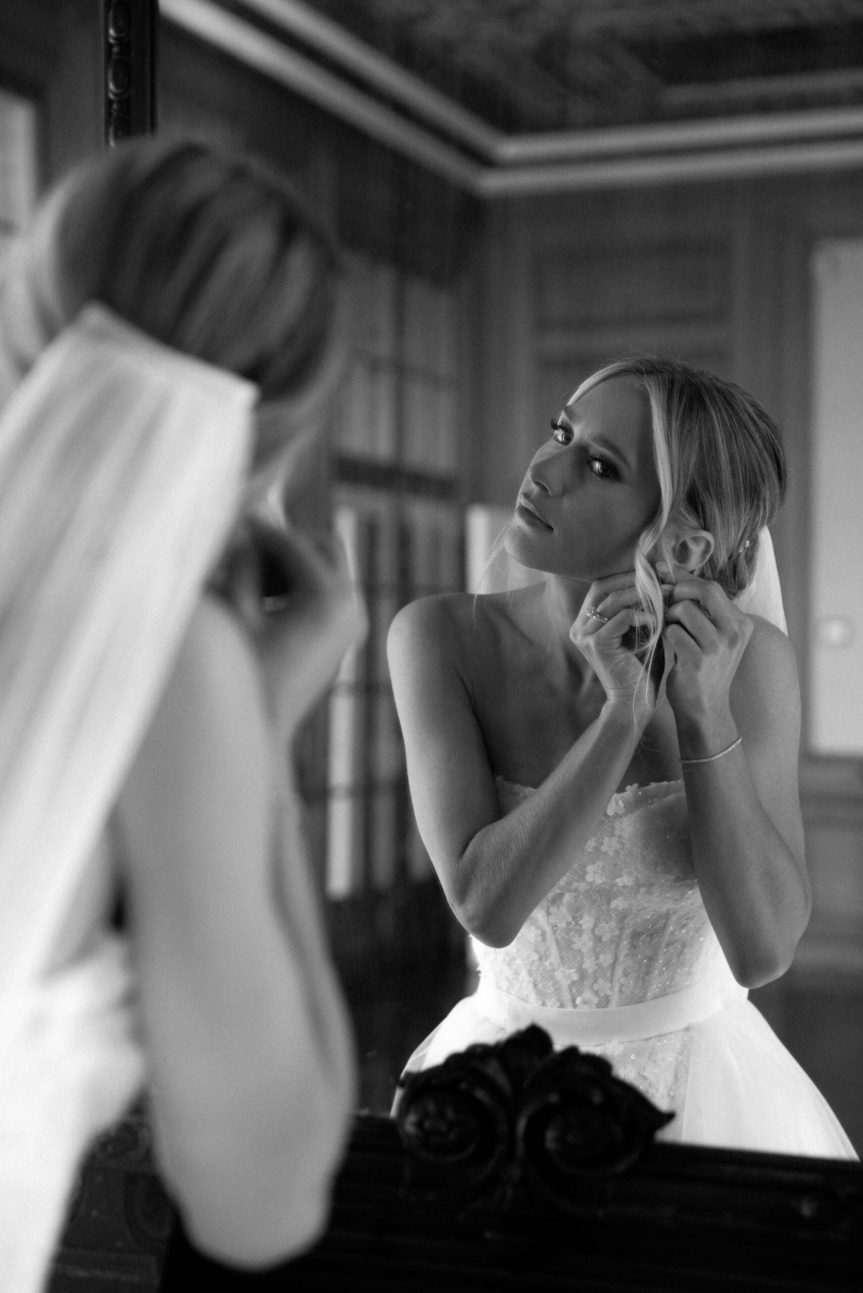 Bride adjusts her earring in front of a mirror, preparing for the wedding.