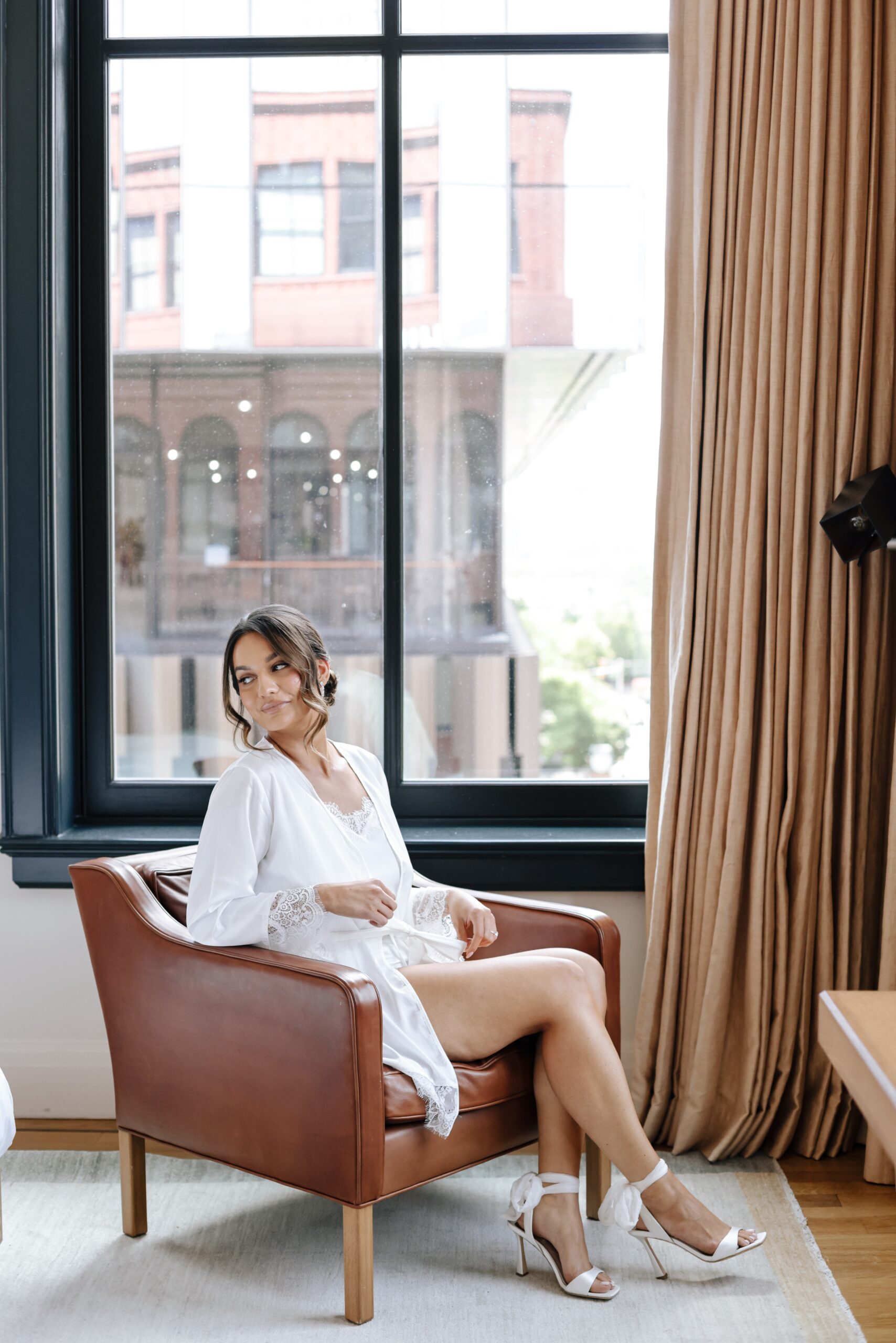 Woman in white robe sitting on a chair by the window.