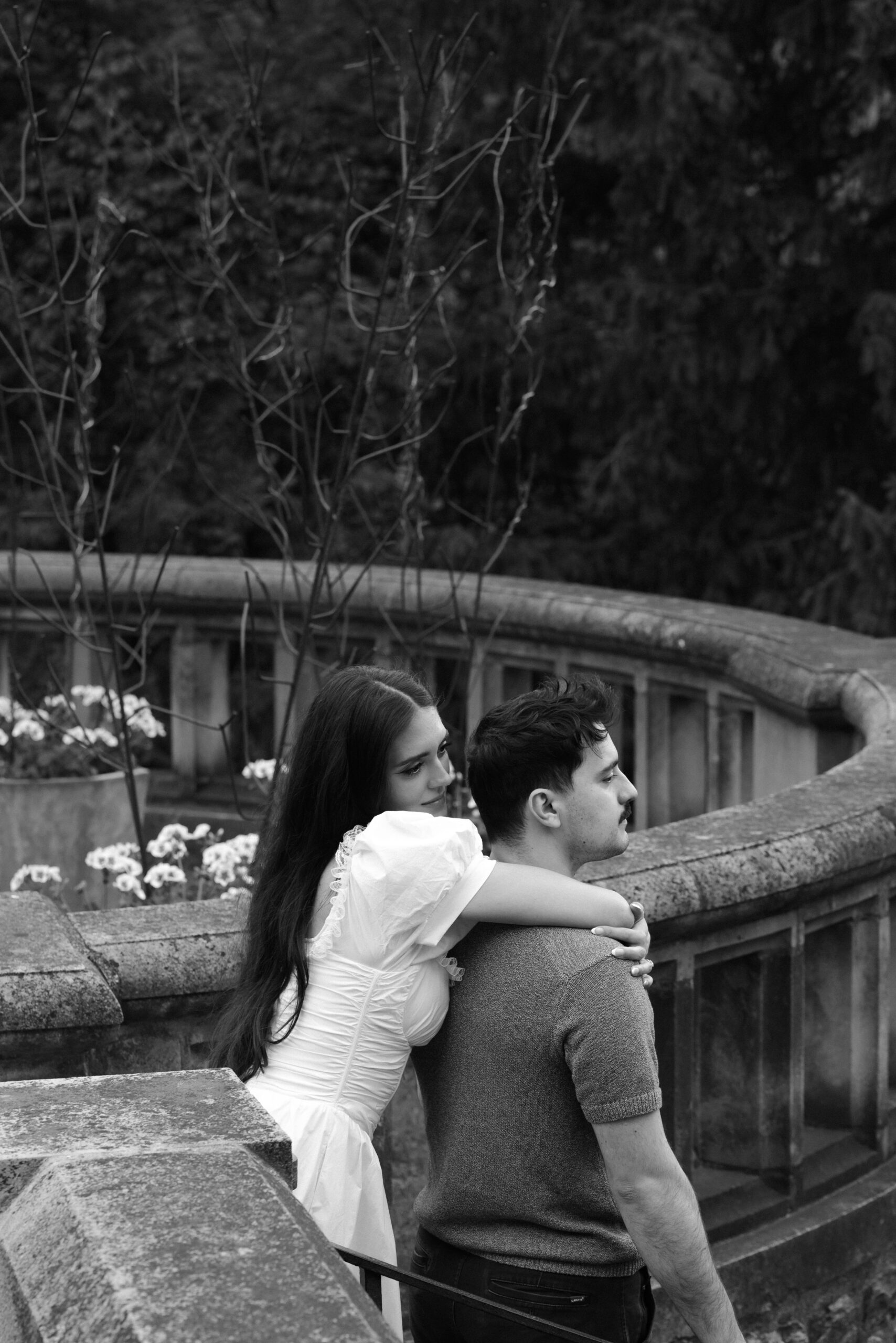Couple embracing outdoors near a curved railing in black and white.