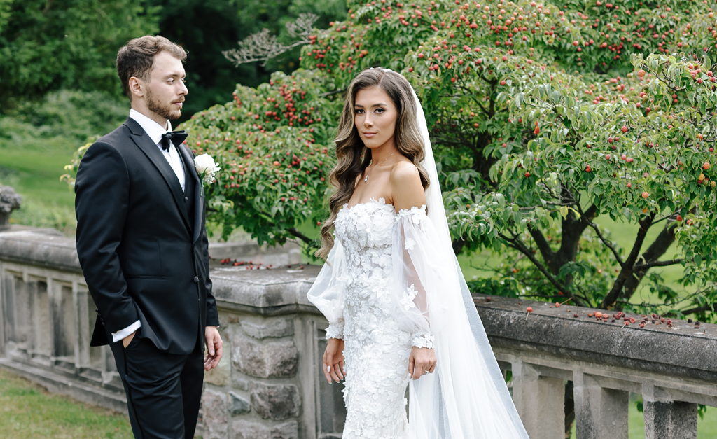 Bride in white gown and groom in tuxedo outdoors.